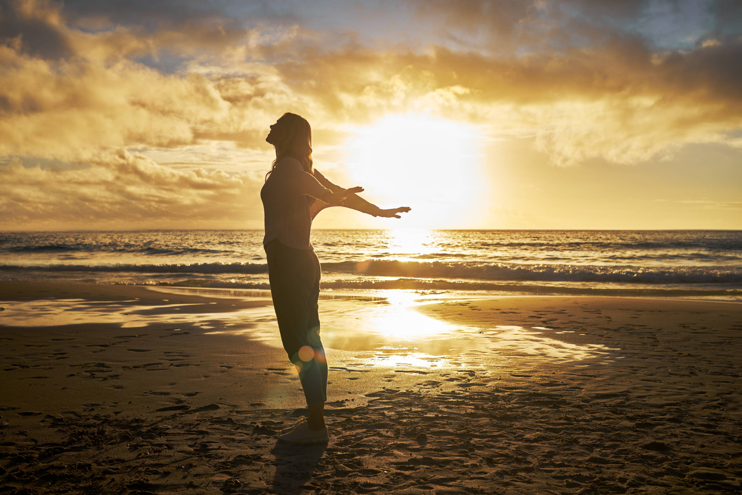 Woman standing on beach at golden sunset with arms wide open - freedom after transformation
